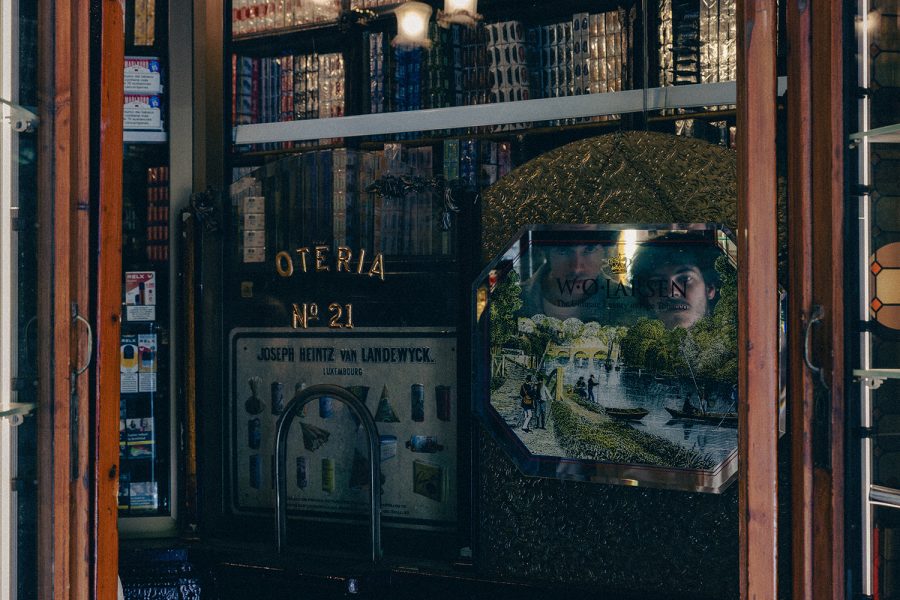 Interior d’un estanc antic amb vitrines de fusta i prestatgeries plenes de capses de tabac. Al centre destaca un expositor decoratiu amb un paisatge imprès i el reflex parcial d’uns rostres al vidre.